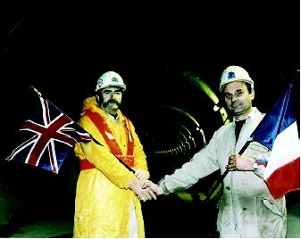 A British and a French worker shake hands at the entrance to the English Channel Tunnel upon its completion in 1990. The "Chunnel" spans 50 kilometers (32 miles) and is submerged beneath the seabed at a varied depth of from 45 meters to 75 meters (150 feet to 250 feet).