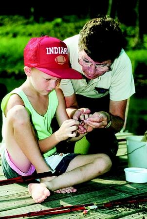 Fresh-water education encompasses surface waters (e.g., lakes, ponds, streams, and wetlands) and groundwaters (e.g., cave, karst, and aquifer systems). Here a young angler learns from a park naturalist how to bait a hook.